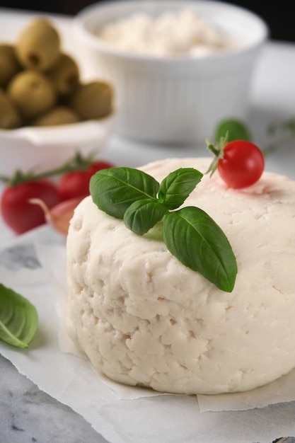 Ricotta cheese Homemade Ricotta cheese with basil garlic tomatoes and green olives on parchment paperback and stand Italian food Selective focus