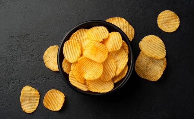 Ridged potato chips in bowl on black background with copy space, top view