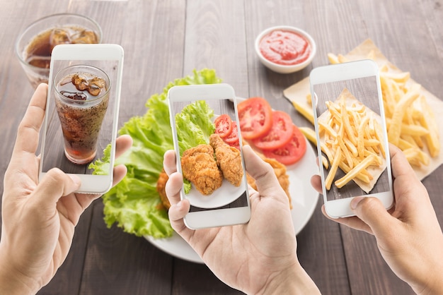 Riends using smartphones to take photos of fried chicken and french fries and cola