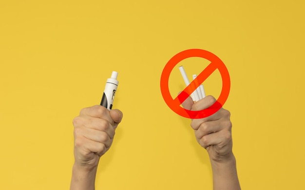 Right hand with vaper and left hand with stop cigars on yellow background