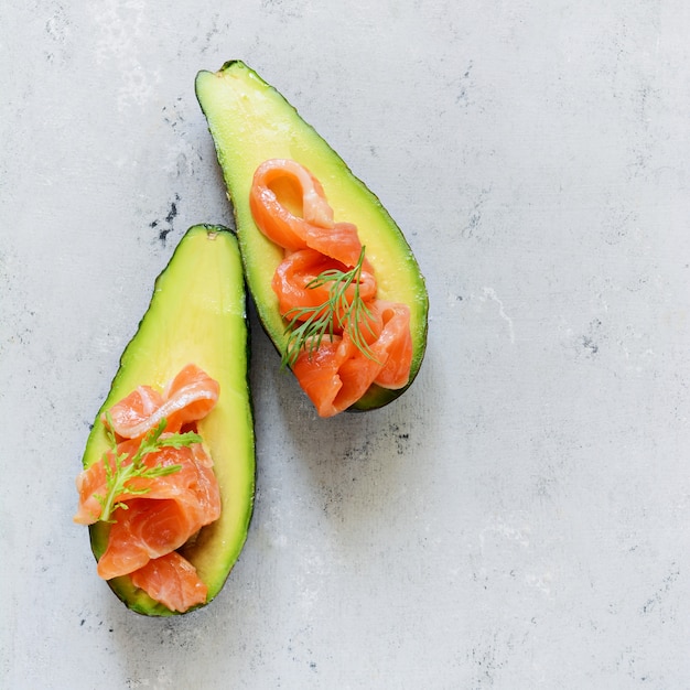 Ripe avocado boats with slices of salted trout, salmon and fresh greens. Avocado boats stuffed with salmon with lime, spinach leaves and arugula, concept healthy food, diet.