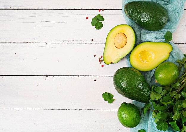 Ripe avocado, lime and cilantro on a wooden table. Healthy food concept. Top view