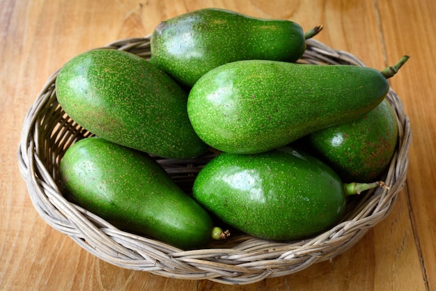 Ripe avocados fruit in basket on wooden table