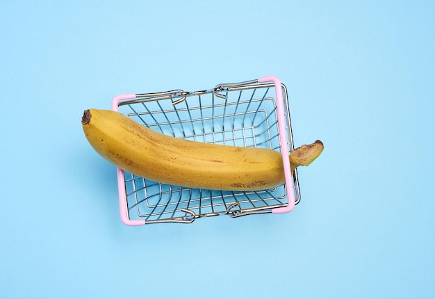 A ripe banana in a miniature shopping cart on a blue background representing the concept of selling fruits and vegetables