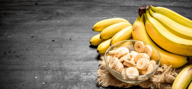 Ripe bananas with pieces of sliced bananas in a bowl . On a black chalkboard.