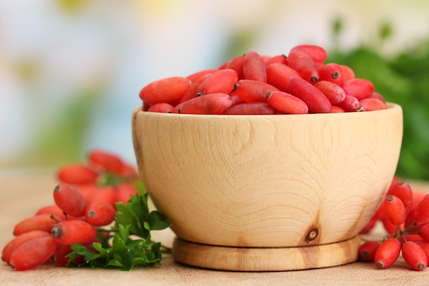 Ripe barberries in wooden bowl with green leaves on table