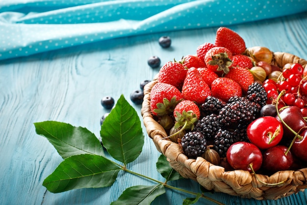 Ripe berries in a wicker plate on a blue wooden table