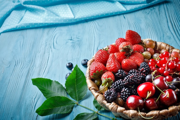 Ripe berries in a wicker plate on a blue wooden table.