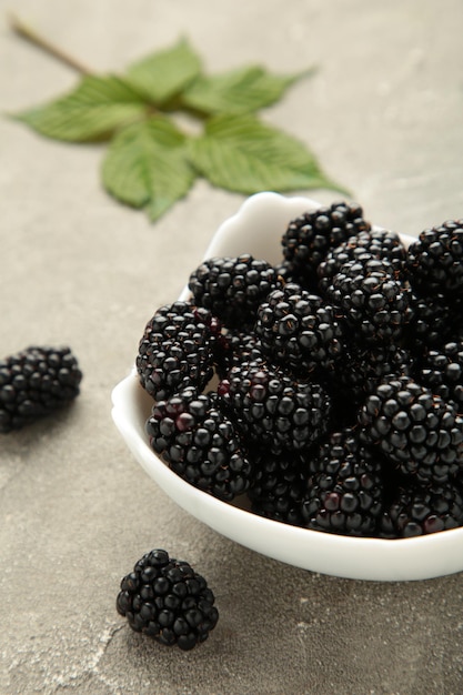 Ripe blackberries with leaves in a white bowl on grey background