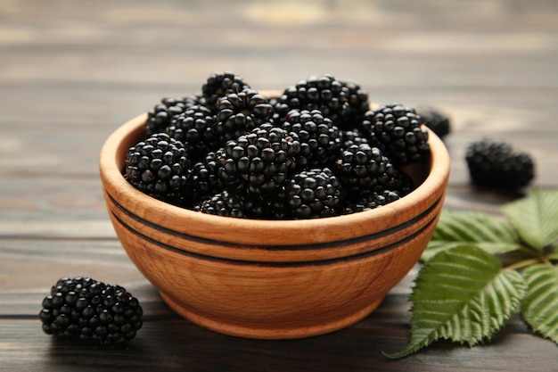 Ripe blackberries with leaves in a wooden bowl on brown wooden background