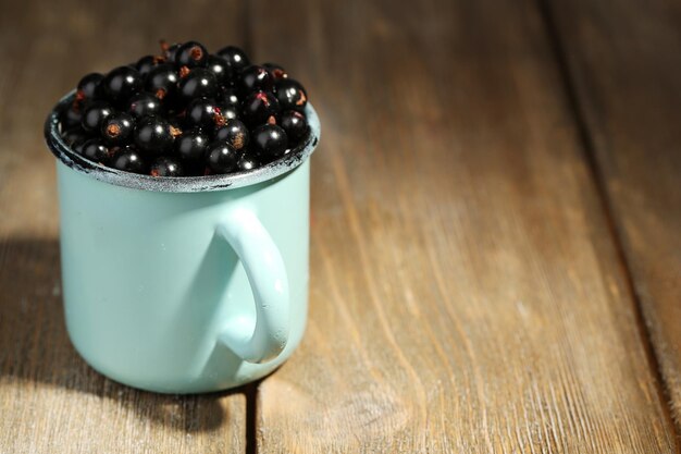 Ripe blackcurrants in mug on wooden background