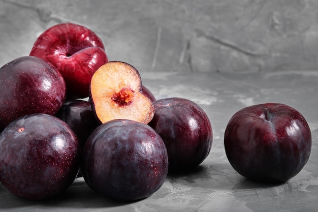 Ripe blue plums lie on a concrete stone table