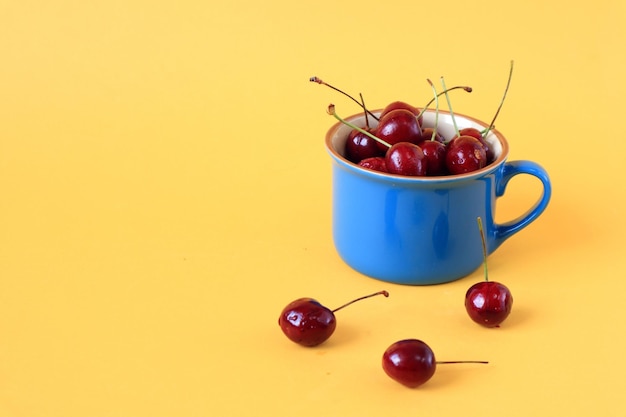 Ripe cherries in a blue cup on a yellow background side view space for text