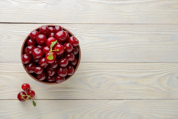 Ripe cherries in a bowl on a textured wooden background, view from above