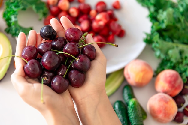 Ripe cherries in female hands on a blurred background of vegetables and fruits