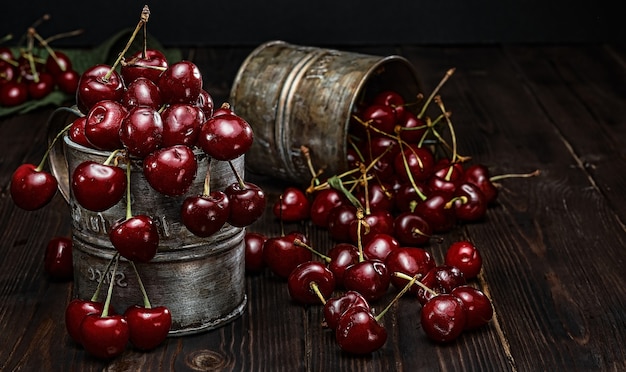 Ripe cherries in vintage metal mugs. Dark wood background, selective focus. Summer cherry picking