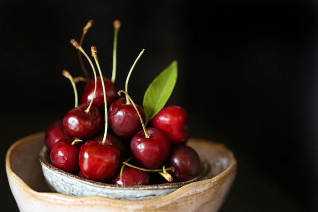 ripe  cherry with leaves in a clay bowl on dark