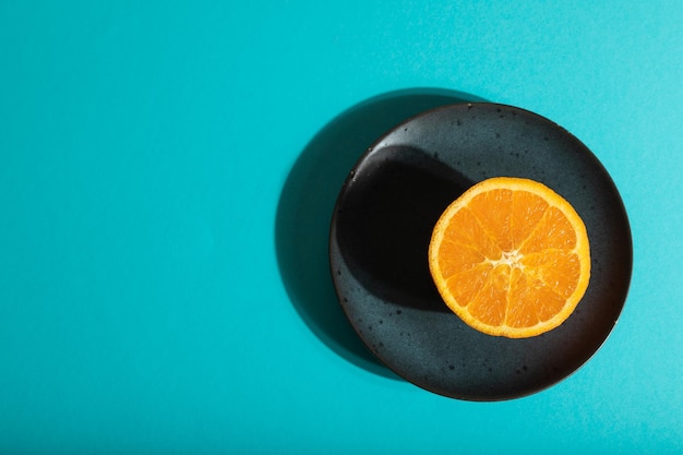 Ripe cut orange on blue ceramic plate on blue pastel background Top view copy space hard light