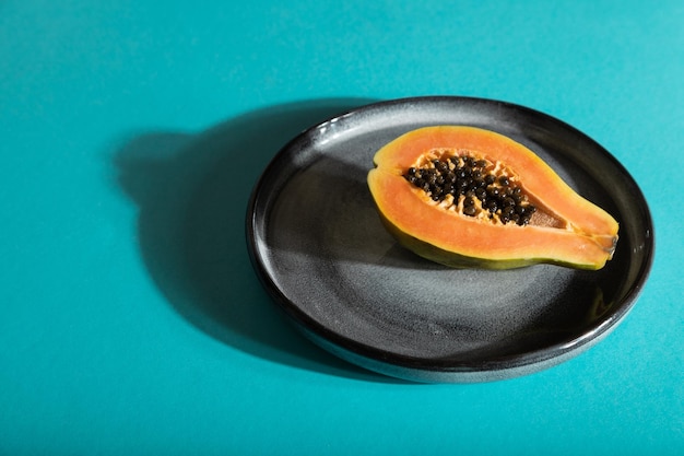 Ripe cut papaya on gray plate on blue pastel background Side view copy space hard light