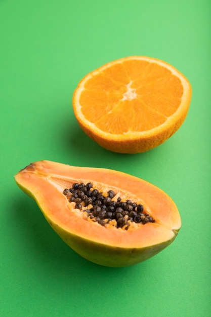 Ripe cut papaya and orange on green pastel background Side view close up