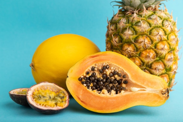 Ripe cut papaya pineapple melon passion fruit on blue pastel background Side view close up