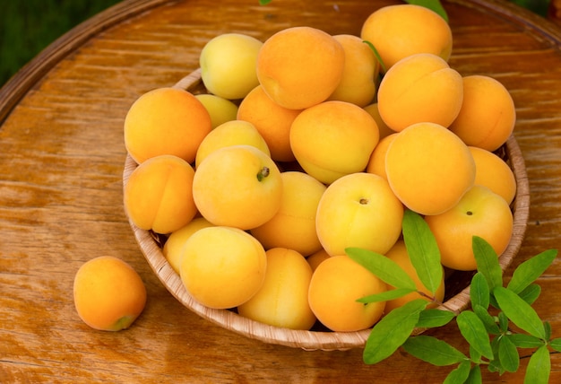 Ripe fresh apricots and leaves in wicker plate on wooden