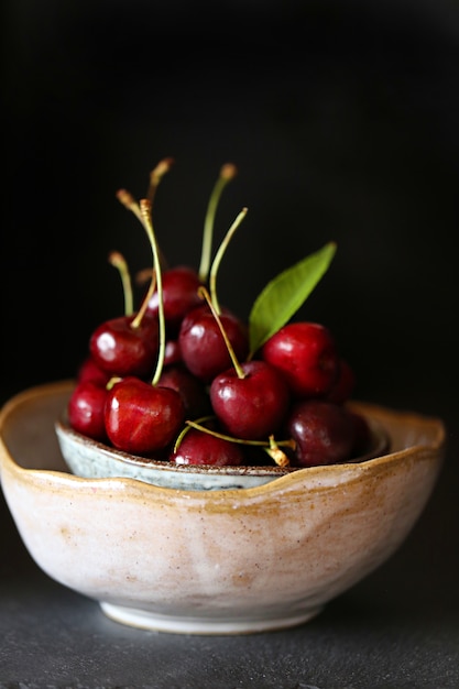 ripe fresh  cherry with leaves in a clay bowl on dark . 