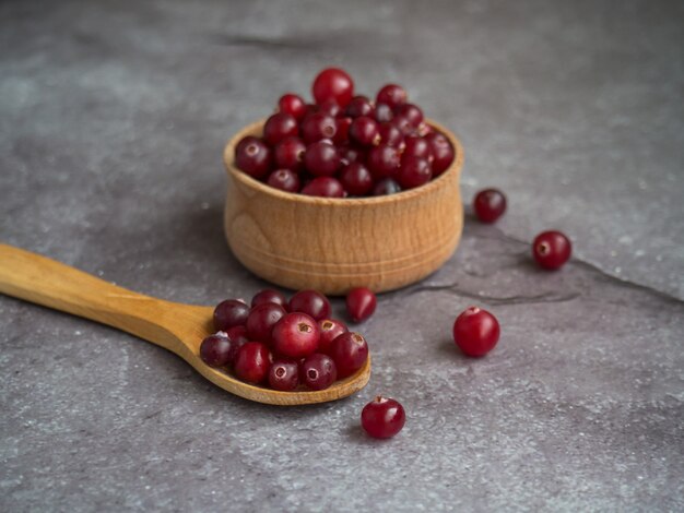 Ripe fresh cranberries in wooden bowl and wooden spoon on concrete table top with copy space