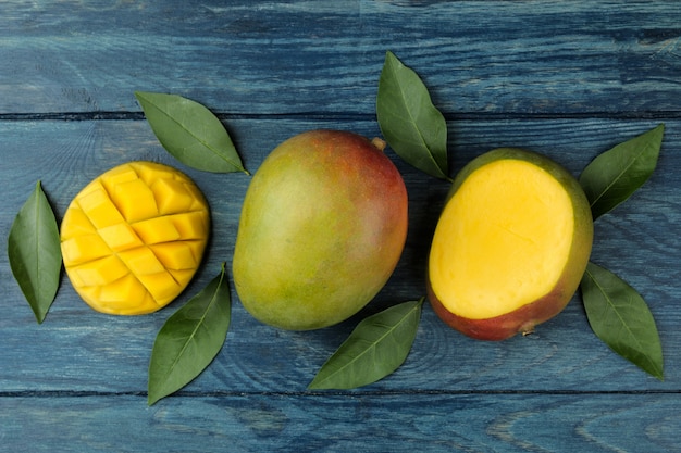 Ripe fresh mango fruit and slices and leaves on a blue wooden table