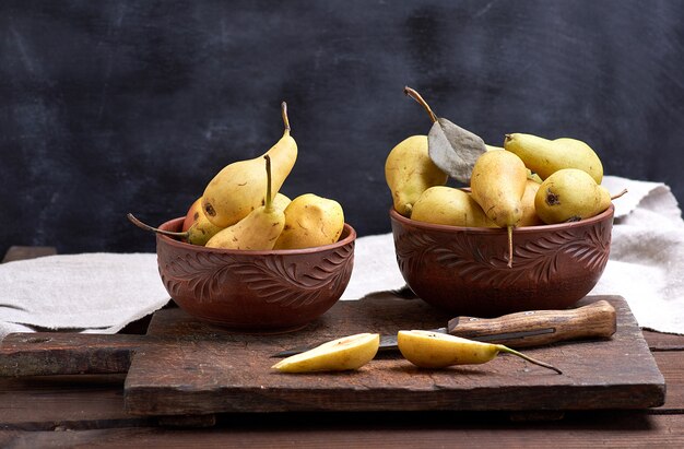 Ripe fresh yellow pears in a clay bowl on brown wooden table