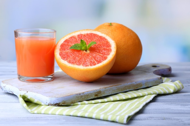 Ripe grapefruits and fresh juice on cutting board on wooden background