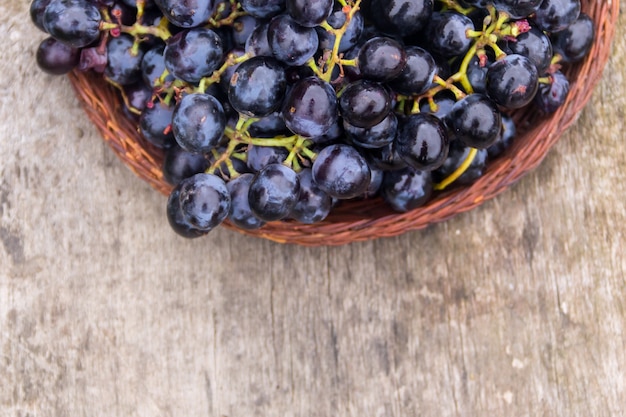 Ripe grapes in wicker basket on wooden table. Top view