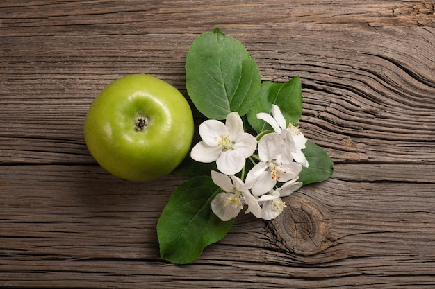 Ripe green apple with branch of white flowers on a wooden table