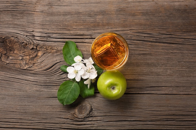 Ripe green apples in wooden box with branch of white flowers and glass of fresh juice on a wooden table. Top view.