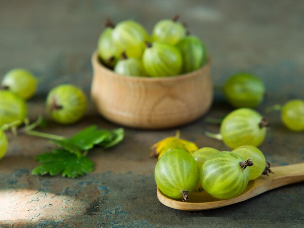 Ripe green gooseberries in a wooden bowl and spoon on an old iron background Vegetarian food