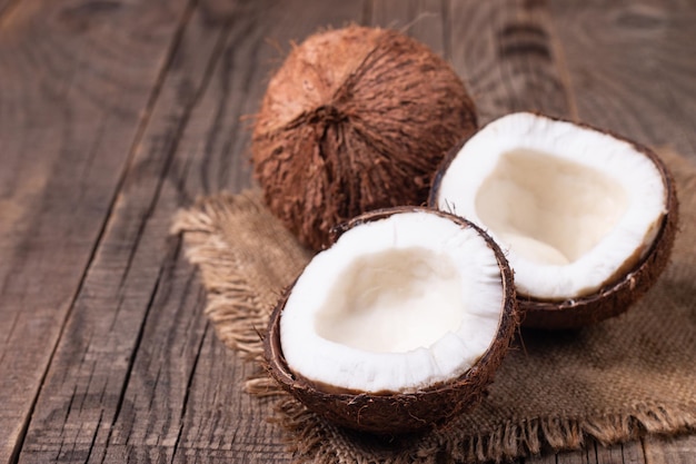 Ripe half cut coconut with green leaves on wooden background.