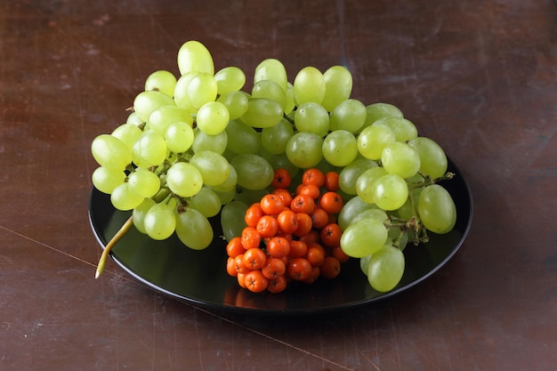 Ripe juicy grapes and rowanberries on a black plate on a dark background Raw and organic fruits harvest from garden closeup