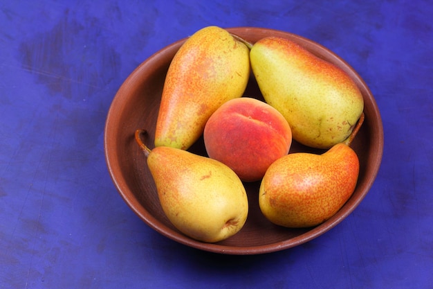 Ripe juicy pears and peach in a clay plate on a blue background Fresh fruits for vegan closeup