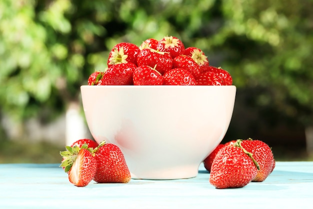 Ripe juicy strawberries in a bowl on a wooden background in the summer garden. Top view