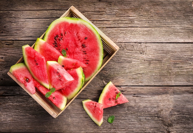 Ripe juicy watermelon pieces in box on wooden background. Top view.