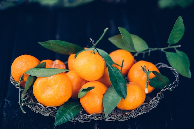 Ripe Mandarin fruit peeled open and place on old rustic look timber with group of mandarin fruits and leaves out of focus on the surface