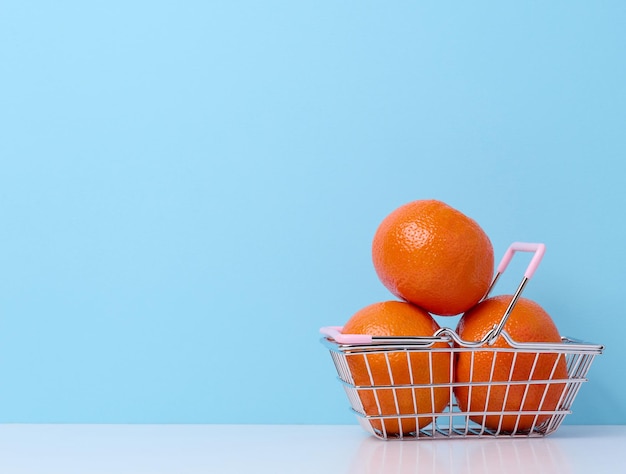 Ripe mandarins in a miniature metal shopping cart on a blue background citrus price increase concept