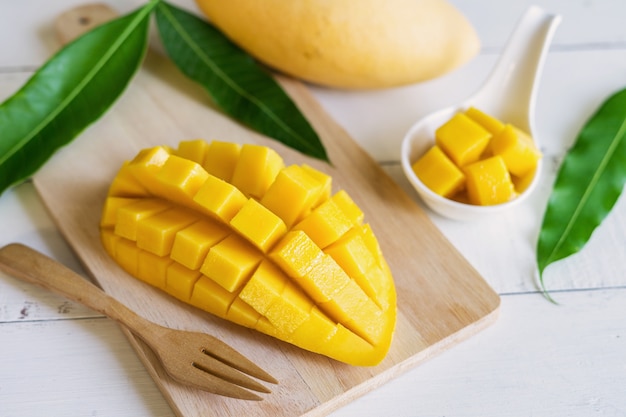 Ripe mango fruit and mango cubes on white wooden table