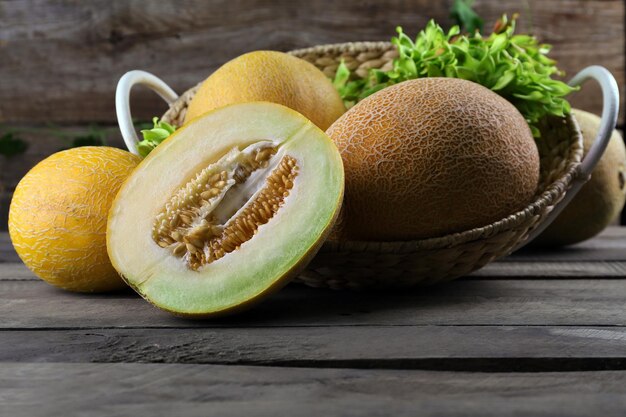 Ripe melons with green leaves in basket on table close up