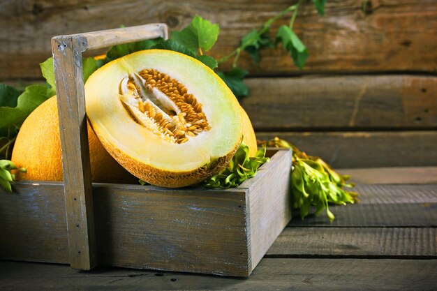 Ripe melons with green leaves in crate on table close up