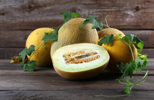 Ripe melons with green leaves on wooden background