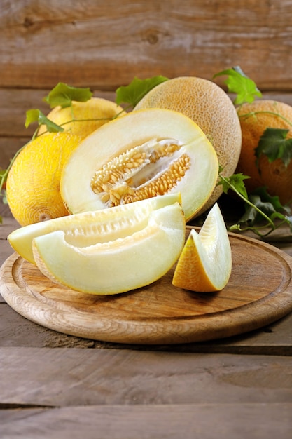 Ripe melons with green leaves on wooden table close up