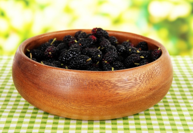 Ripe mulberries in bowl on table on bright background