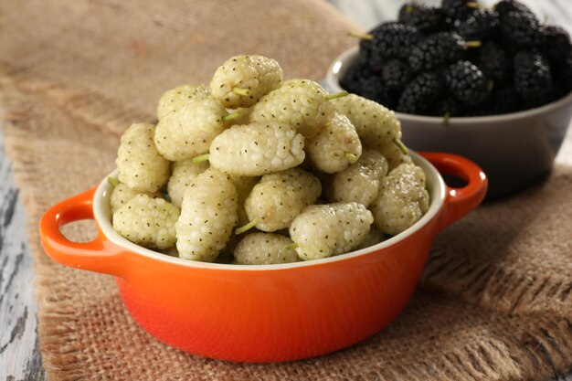 Ripe mulberries in bowls on table close up