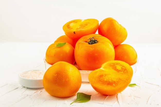 Ripe orange tomatoes with fresh basil. New harvest vegetables on a ceramic stand. White putty background, close up